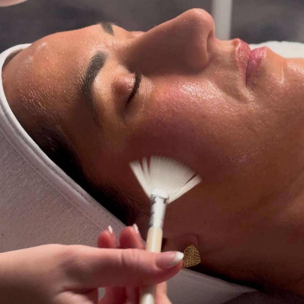 Person receiving a facial treatment with a brush applying product to their face.
